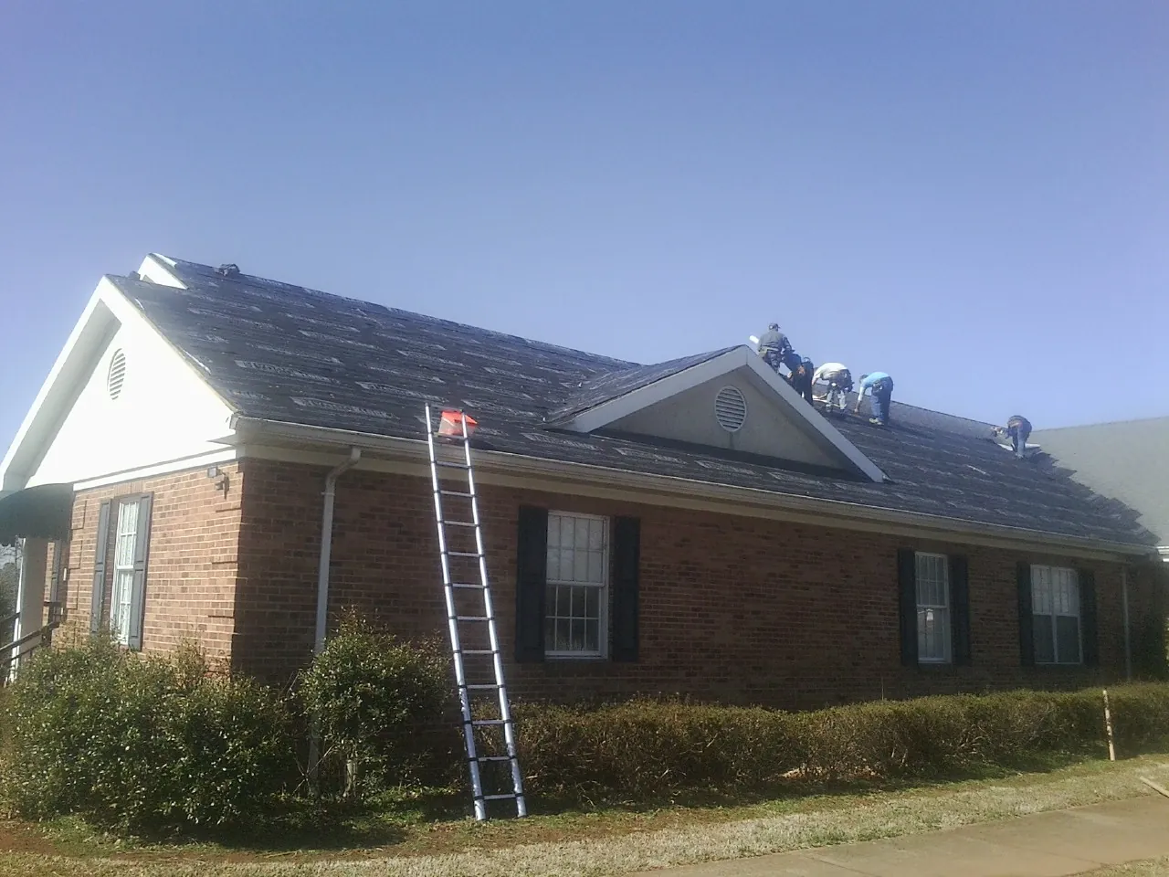 Crew tearing shingles off a brick ranch roof with a ladder set — Emergency Roof Repair work by our crew in Aneta