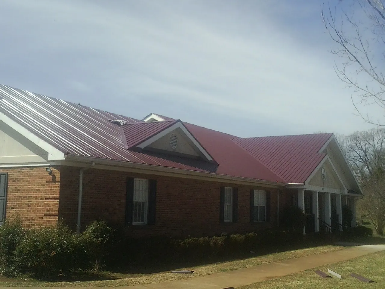 Red metal roof with gabled entries on a long brick building, from a Hail Damage Roof Repair job in Aneta