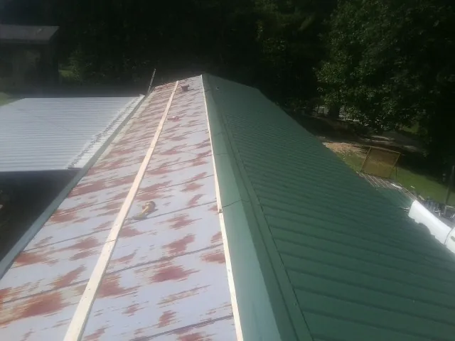 Old rusted panels beside newly installed green metal roofing — Wind Damage Roof Repair by Roofing Brothers in Aneta