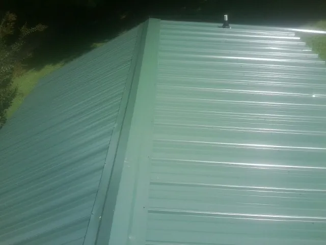 New green metal panels meeting at the ridge of a roof — Flat Roof Repair work by our crew in Aneta