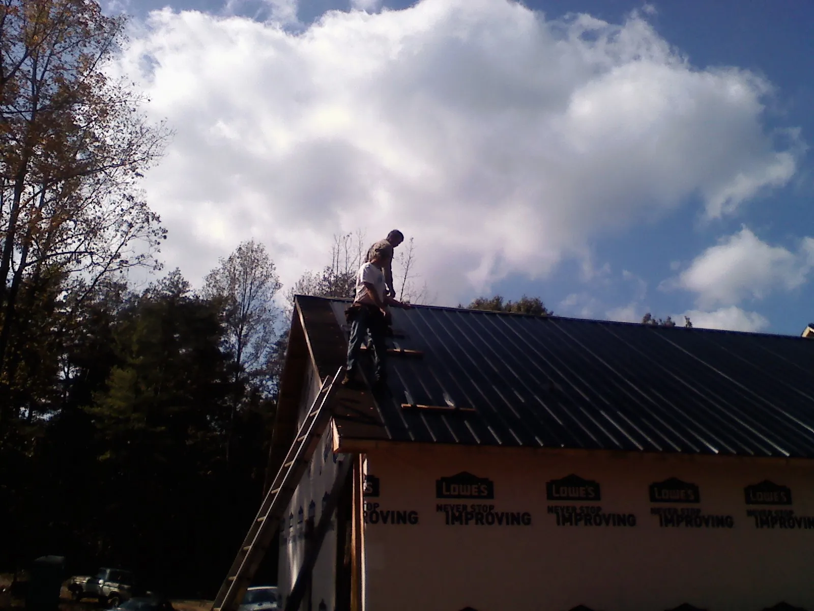 Roofer fastening dark metal panels high against a cloudy sky, from a Roof Inspection job in Aneta