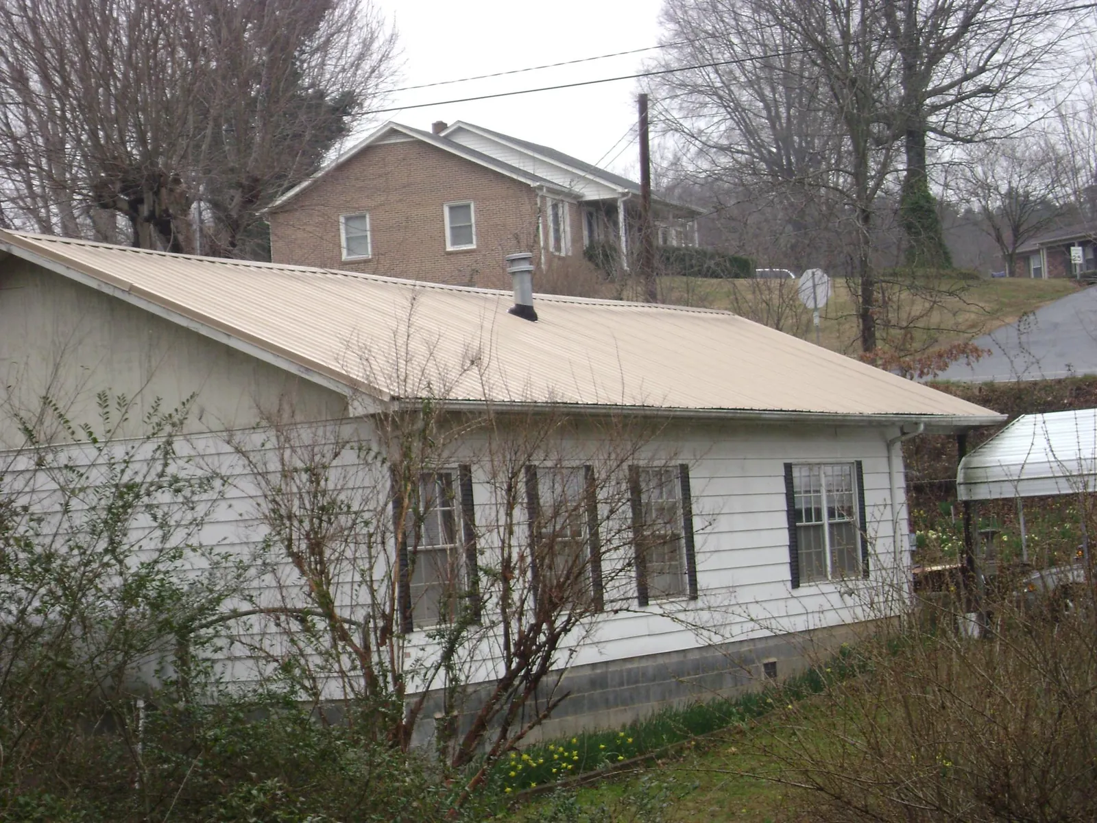 Tan metal roof on a white sided house set into a hillside — Commercial Roofing by Roofing Brothers in Aneta