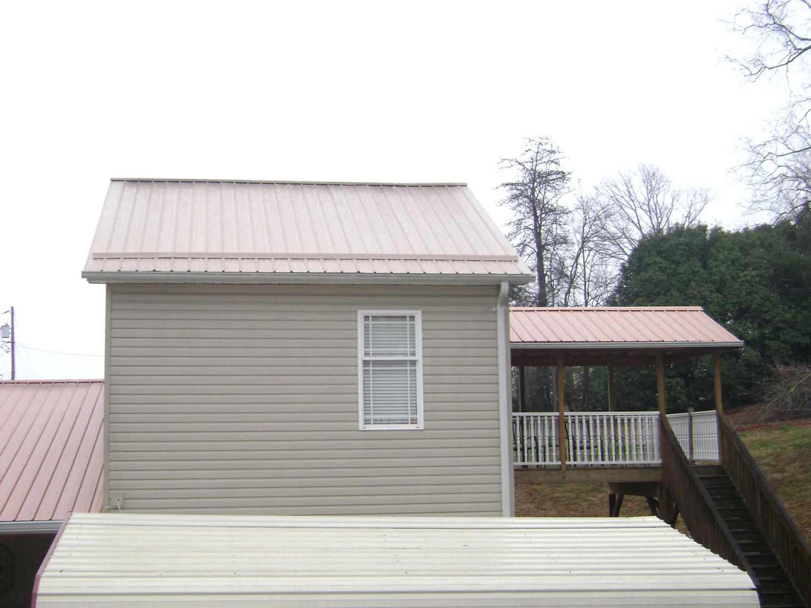 Tan metal roofs on a two story addition and attached porch, from a Roof Replacement job in Aneta